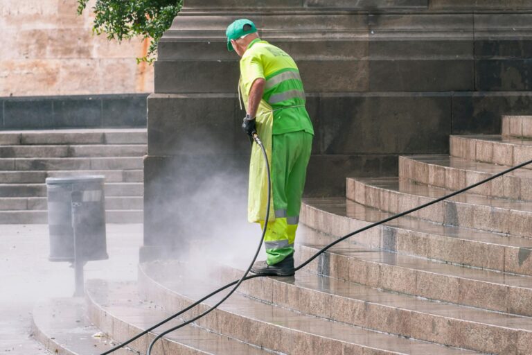 A street worker pressure washes stone stairs in a public park, ensuring cleanliness and safety.